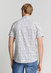 Korte mouwen overhemd met knopen, gemaakt van een witte stof met een herhalend patroon van donkere en lichte ovale vormen. Casual pasvorm met een omgeslagen kraag.