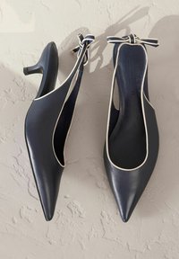 Navy nahka slingback-korkokengät, joissa on terävät kärjet ja valkoiset koristeet, matalalla korolla ja rusettiyksityiskohtana takana.