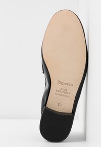Semelle de chaussure en cuir noir avec une texture lisse. Comprend un logo estampé et la taille "37". La partie inférieure beige clair présente une finition contrastante.