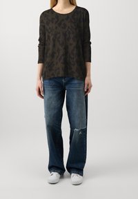 Maglione verde oliva scuro con stampa leopardata nera, abbinato a jeans a gamba larga blu sbiaditi con strappi e sneakers bianche.