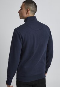 Mørkeblå sweatshirt med h�øy krage, ribbestrikkede mansjetter og nederkant. Glatt tekstur og lett glans, med minimale søm detaljer.
