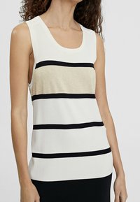 Donna che indossa un top senza maniche bianco con righe orizzontali nere e una striscia beige testurizzata sulla parte centrale del petto.