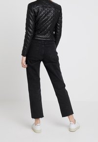 Veste en cuir noir matelassée avec des manches ajustées, associée à un jean noir taille haute et des baskets blanches. Présente un ourlet effiloché sur le jean.