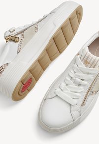 Λευκά sneakers χαμηλής κοπής με μπεζ υφασμάτινες λεπτομέρειες, χρυσά πλαϊνά φερμουάρ, λευκά κορδόνια και ανοιχτοκαφέ λαστιχένιες σόλες με αντίστοιχα σχέδια.