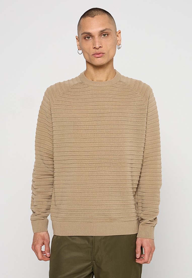 Suéter de punto acanalado en color beige con cuello redondo, rayas horizontales texturizadas y corte relajado. Cuenta con mangas largas y puños acanalados.