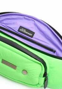 Groene gevoerde tas met een paarse binnenkant, een zwarte rits en een logo-patch. Opmerkelijke hardware omvat een hexagonaal accent en metalen studs.