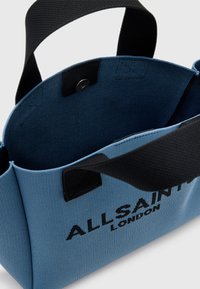 Niebieska torba materiałowa z czarnymi akcentami, wyposażona w dwie solidne uchwyty, górne zapięcie na zatrzask i napis "ALLSAINTS LONDON" w kolorze czarnym.