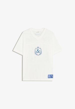 Biały, siatkowy T-shirt z krótkim rękawem i dekoltem w serek, z niebieskim ozdobnym symbolem ampersanda na piersi oraz niebieską prostokątną metką w pobliżu dolnego brzegu.