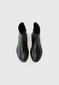 Botas negras de cuero hasta el tobillo con una textura suave, punta redondeada y cremallera lateral. La suela cuenta con un ligero relieve para mayor tracción.