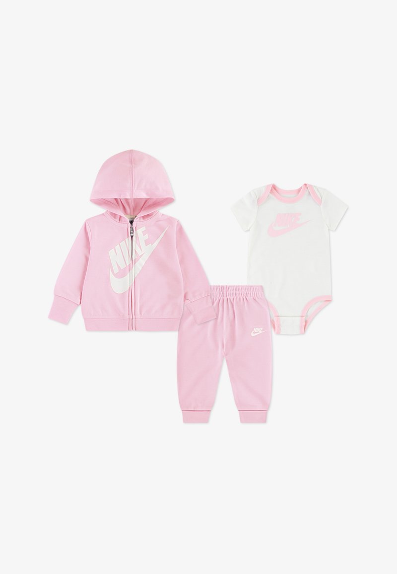 Roza otroška obleka, ki vključuje zadrgo na kapucarju z belim logotipom Nike, usklajene trenirka hlače ter belo bodi majico z roza obrobami in logotipom.