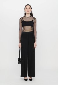 Haut long à manches longues en dentelle noire superposé à un débardeur noir ajusté, associé à un pantalon large taille haute noir et des escarpins noirs à bout pointu.