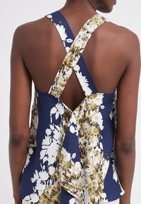 Marinblomstrig blus med korsettryggdesign, i en strukturerad tyg med vita blommönster som accentueras av grönt. Bakstycket har en draperad detalj.