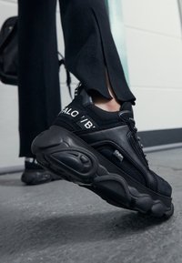 Baskets de sport noires avec dessus texturé, semelle épaisse et logo bien visible sur le côté. Dotées de lacets et d'un design en maille distinctif.