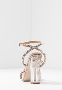 Högklackad sandal med en klar blockklack, nakenremmar prydda med rhinestones och korsade ankelremmar för säker passform.