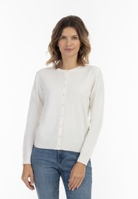 Cardigan bianco in maglia con scollatura tonda, dotato di chiusura a bottoni sul davanti, polsini a costine e una texture liscia. Abbinato a jeans blu.
