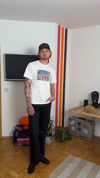 Camiseta blanca con un gráfico vibrante de Levi's, pantalones negros y zapatos burdeos. La habitación presenta rayas coloridas y elementos decorativos.