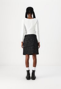 Haut blanc à manches longues associé à une jupe en tweed noir texturé. La tenue présente une silhouette ajustée et des bottines noires à la cheville avec un revers.