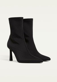 Bottines noires en tissu lisse, avec un bout pointu, une tige ajustée et un talon haut et élancé. Design épuré et minimaliste.