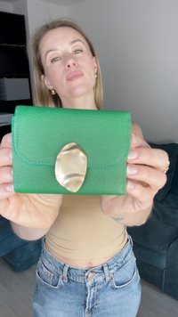 Green textured leather wallet with a curved gold clasp. Compact design with rounded corners and pronounced stitching details.