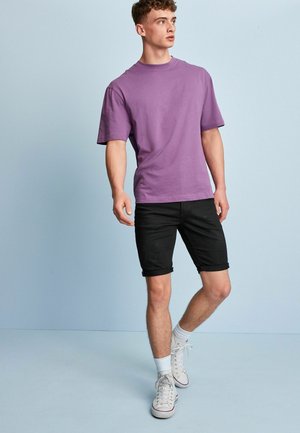 Fialové bavlnené tričko s krátkymi rukávmi, skombinované s zvieranými čiernymi denimovými šortkami. Model má na sebe biele tenisky a členkové ponožky.
