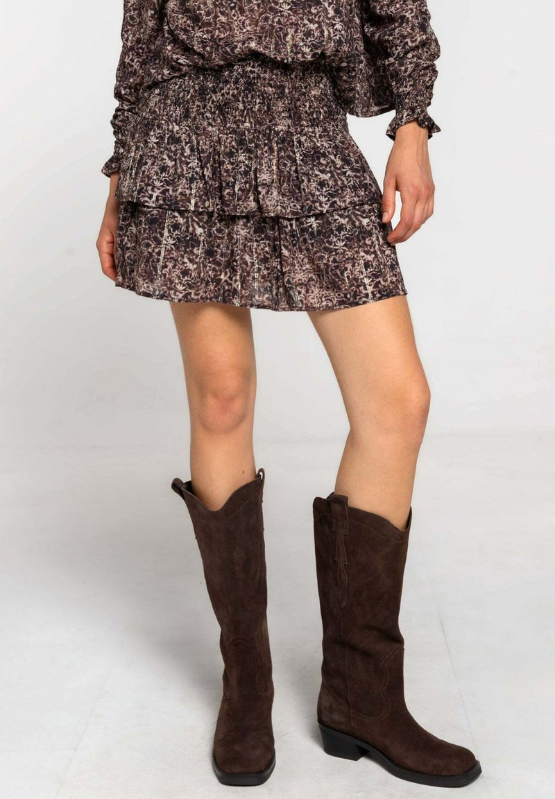 Jupe imprimée en dégradé, de couleur brun clair, confectionnée en tissu texturé, assortie à des bottes en daim marron foncé, mi-mollet, avec un léger talon.