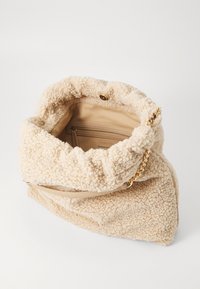 Beige, fluffig väska gjord av texturerad tyg, med en guldkedja som axelrem, en knappstängning, och ett slätt innerfack för organisering.