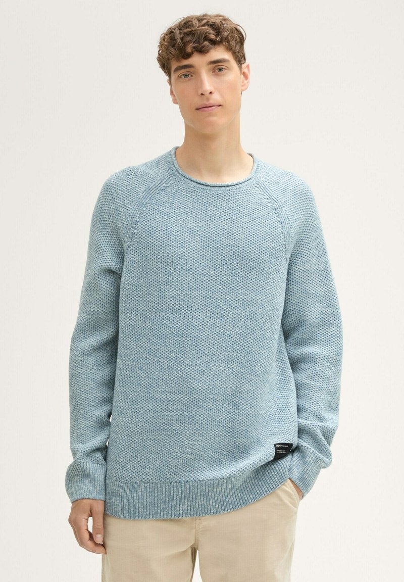 Hellblauer Strickpullover mit strukturiertem Muster, gerippten Bündchen und Saum. Mit Raglanärmeln und einem kleinen Etikett an der Seite.