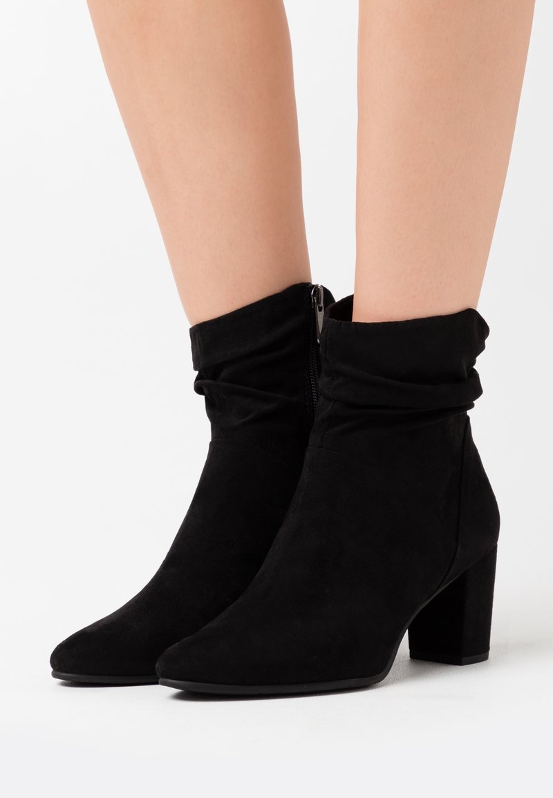 Bottines en daim noir avec une tige légèrement froissée, un bout rond et un talon bloc. Détail de fermeture éclair latérale apparente pour un enfilage facile.