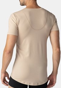 Krémová košile s krátkým rukávem a zakřiveným švem na zádech, vyrobená z hladkého materiálu. Má zaoblený výstřih a delší lem.