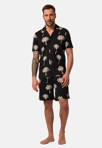 Conjunto de camisa de manga corta negra y pantalones cortos con un estampado de palmeras en beige. El material parece ligero; el patrón se repite en ambas piezas.
