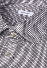 Camicia a motivo in bianco e marrone, con design geometrico. Colletto con chiusura a bottoni, tessuto morbido e etichetta cucita.