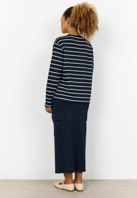 Navy striped long-sleeve top with white lines, paired with a navy midi skirt featuring side pockets; worn with beige shoes.