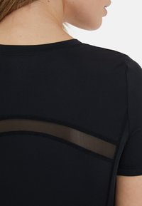 Čierny športový top s krátkymi rukávmi, priliehavým strihom a sieťovinovým panelom na hornej časti chrbta. Hladká textúra s kontrastným šitím.