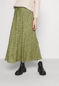 Gonna verde con motivo a foglie nere, design fluido, realizzata in tessuto leggero. Abbinata a stivaletti neri dal design robusto.