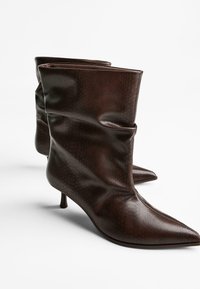 Cizme cu model de șarpe maro, până la gleznă, cu vârful ascuțit și toc subțire, înalt. Realizate din piele netedă, cu un design lejer.
