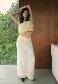 Beige ruffled crop top yhdistettynä pitkään, vaalean kermaiseen hameeseen, jossa on naru vyötäröllä ja kerroksellinen kangas. Teräväkärkiset mustat korkokengät sopivat asusteena.