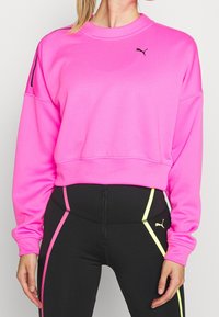 Felpa fucsia brillante con scollo a girocollo e spalle scese. Logo nero sul petto, caratterizzato da accenti a contrasto in nero e giallo sui leggings.