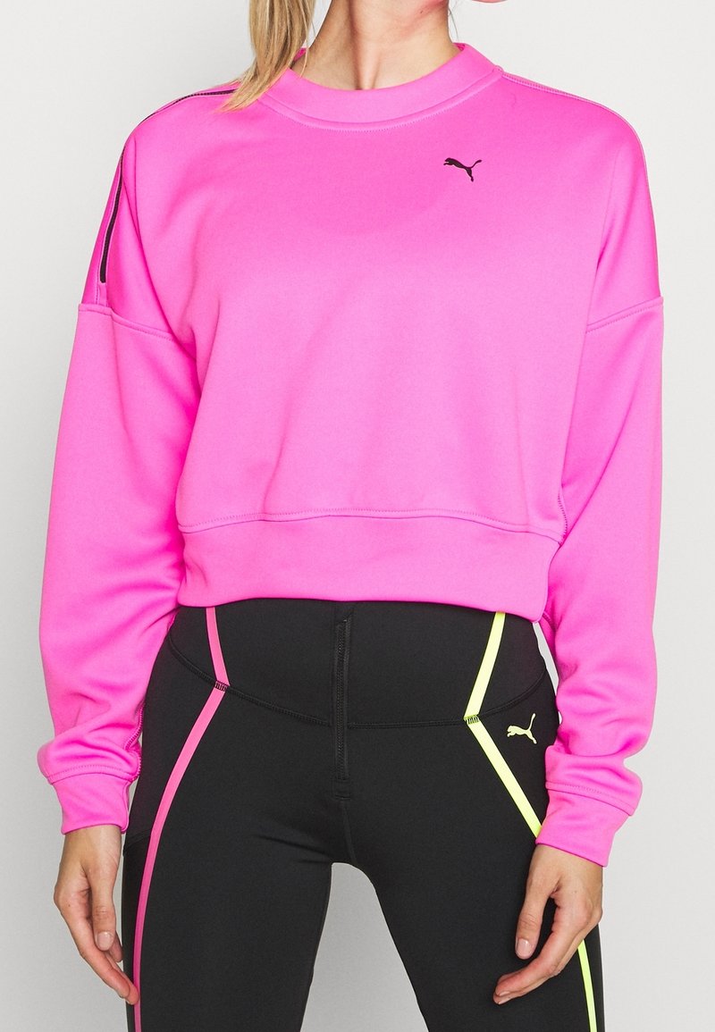 Felpa fucsia brillante con scollo a girocollo e spalle scese. Logo nero sul petto, caratterizzato da accenti a contrasto in nero e giallo sui leggings.