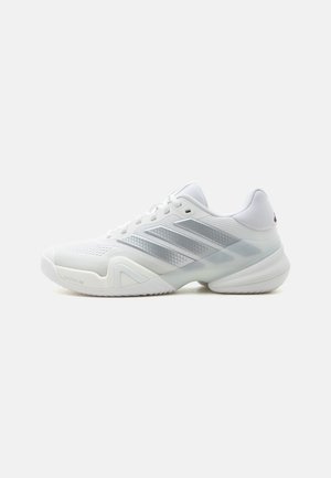 Weißer, niedrig geschnittener Sportschuh mit grauen Adidas-Streifen, Mesh-Obermaterial, gepolsterter Sohle und Schnürverschluss, von der Außenseite gezeigt.