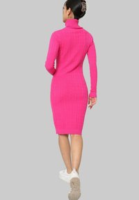 Robe en turtleneck ajustée et côtelée de couleur rose vif, longueur genou avec des manches longues, arborant un motif texturé et des poignets, associée à des baskets blanches.