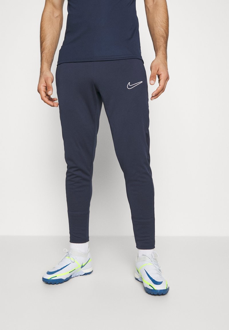 Donkerblauwe Nike trainingsbroek met taps toelopende pijpen en logodetail. Gecombineerd met grijze en blauwe sportschoenen met neon accenten. Gemaakt van een katoenmix.