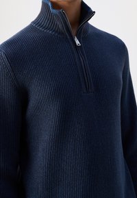 Maglione a costine blu navy con collo a mezza zip, caratterizzato da tessuto testurizzato e design aderente. Il collo superiore è di una tonalità leggermente più chiara.