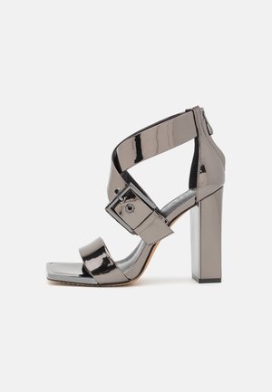 Sandały na obcasie w metalicznej szarości z lakierowanej skóry, z kwadratowym noskiem, szerokimi paskami i masywnym słupkowym obcasem. Obecny jest także regulowany zamek.