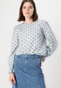 Blusa azul clara com padrão floral, tecido suave, mangas longas bufantes, combinada com saia de jeans de cintura alta com fenda frontal e detalhe em botão.