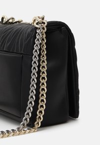 Sac en cuir matelassé noir de forme rectangulaire. Doté d'une bandoulière à chaîne bicolore en argent et en or, mettant en valeur la texture et le design.
