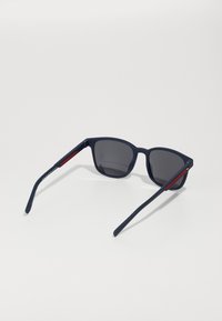Ochelari de soare bleu marin cu lentile întunecate, formă rectangulară, finisaj mat și accente roșii pe brațe. Material de plastic de înaltă calitate.