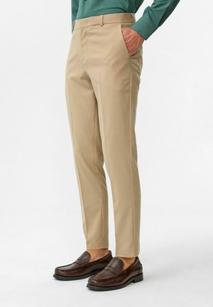 Beige pantalon op maat gemaakt van soepele stof, met een vlakke voorkant en zijzakken, gecombineerd met donkerbruine instappers.