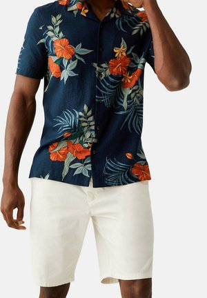 Camicia a maniche corte blu navy con motivo floreale rosso e arancione, bottoni neri e vestibilità comoda, abbinata a pantaloni corti bianchi.
