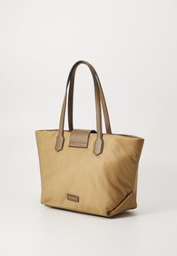 Sac fourre-tout avec un extérieur en nylon beige, texture lisse, et des accents en cuir marron. Dispose d'une poignée plate et d'une fermeture à rabat avec un patch logo.