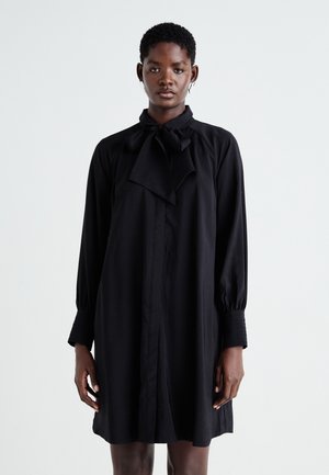 Black long-sleeve dress with a bow tie at the neck, featuring a straight cut, button front, and textured sleeves. Soft, smooth fabric.